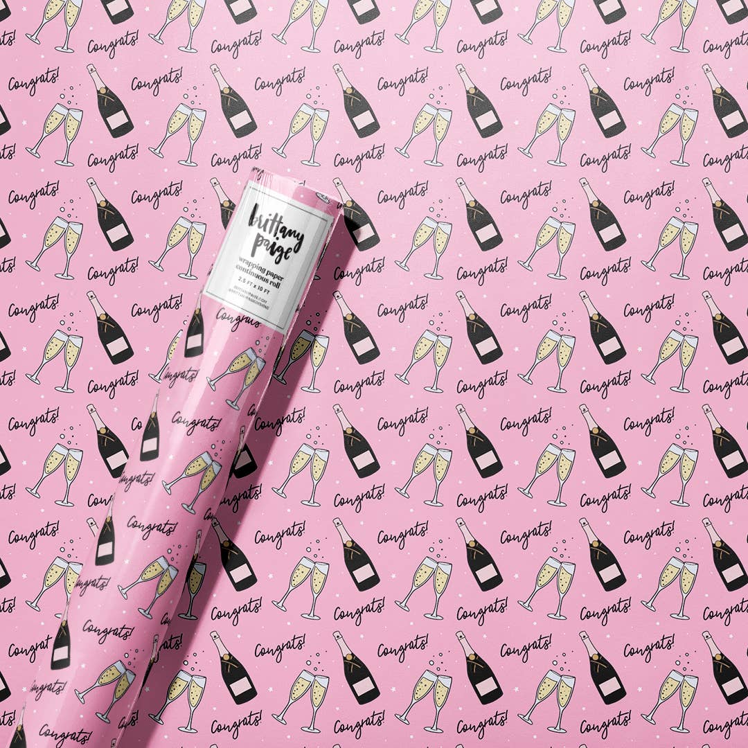 roll of wrapping paper that has a pink background with a continuous pattern of a champagne bottle, two flutes clinking and the text "congrats" all over