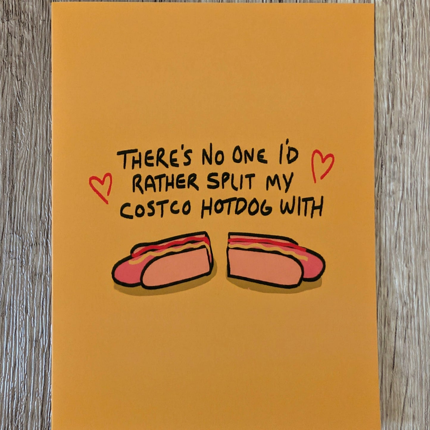 mustard colored card with text in the center that reads "There's no one I'd rather split my Costco hotdog with" and an image with a split hotdog