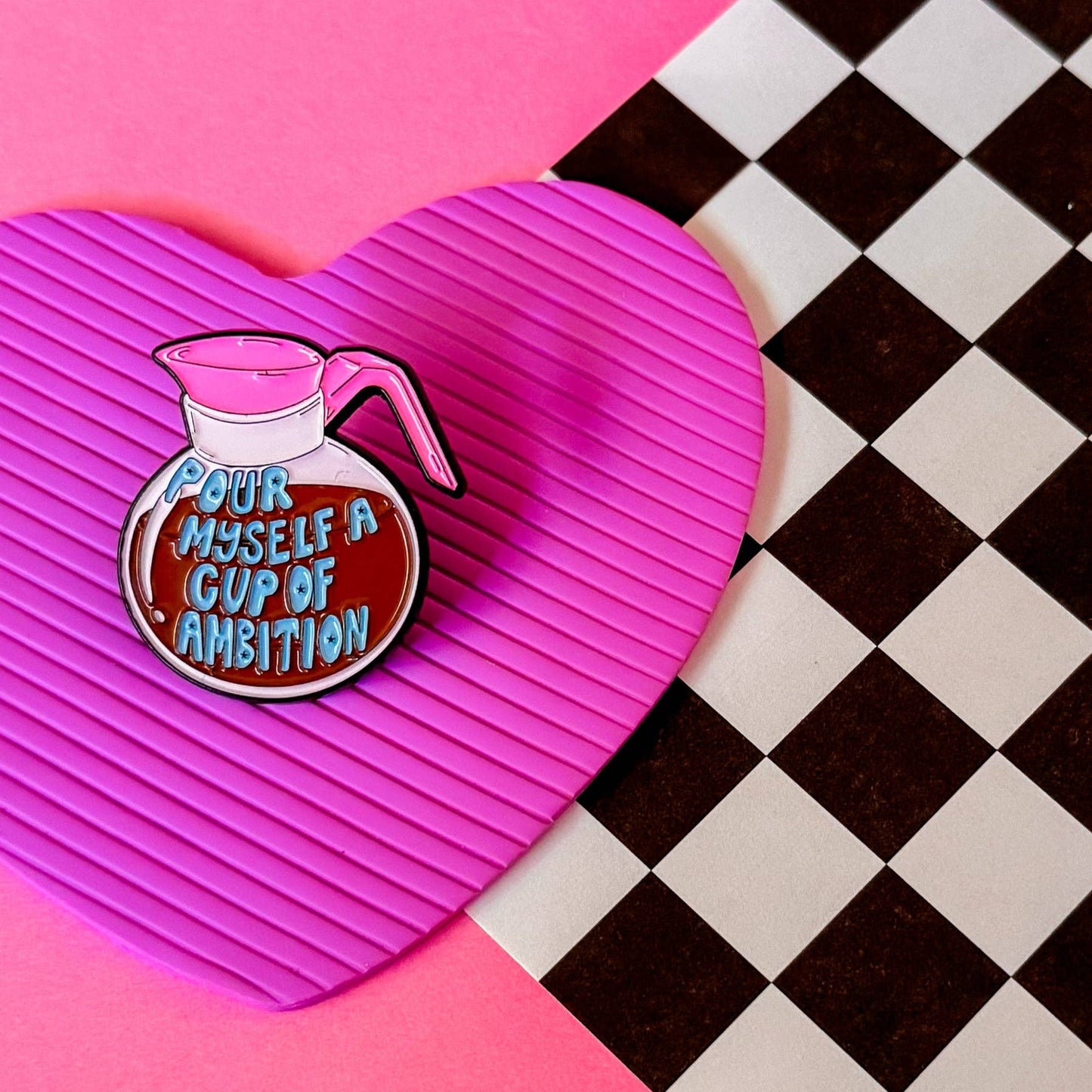 Enamel pin with coffee pot design and text that says "Pour myself a cup of ambition" on a pink heart-shaped background