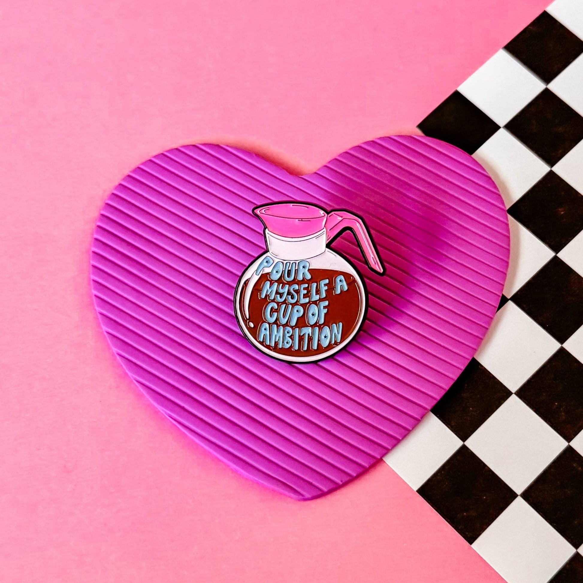 Heart-shaped pink coaster with a coffee pot design enamel pin on a pink and black checkered background