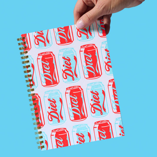 Notebook with Diet Coke can design held by a hand against a blue background