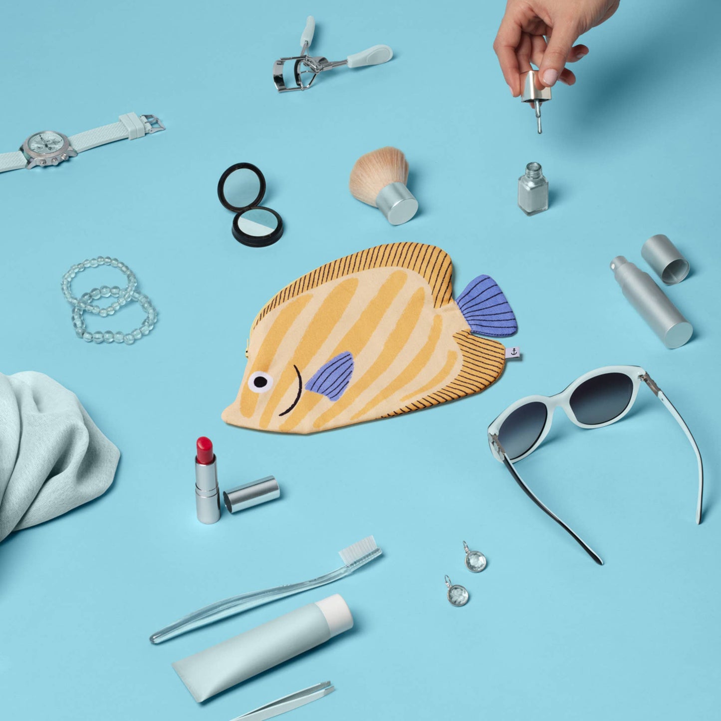 Collection of small items including a fish-shaped pouch, sunglasses, and lip products on a blue background