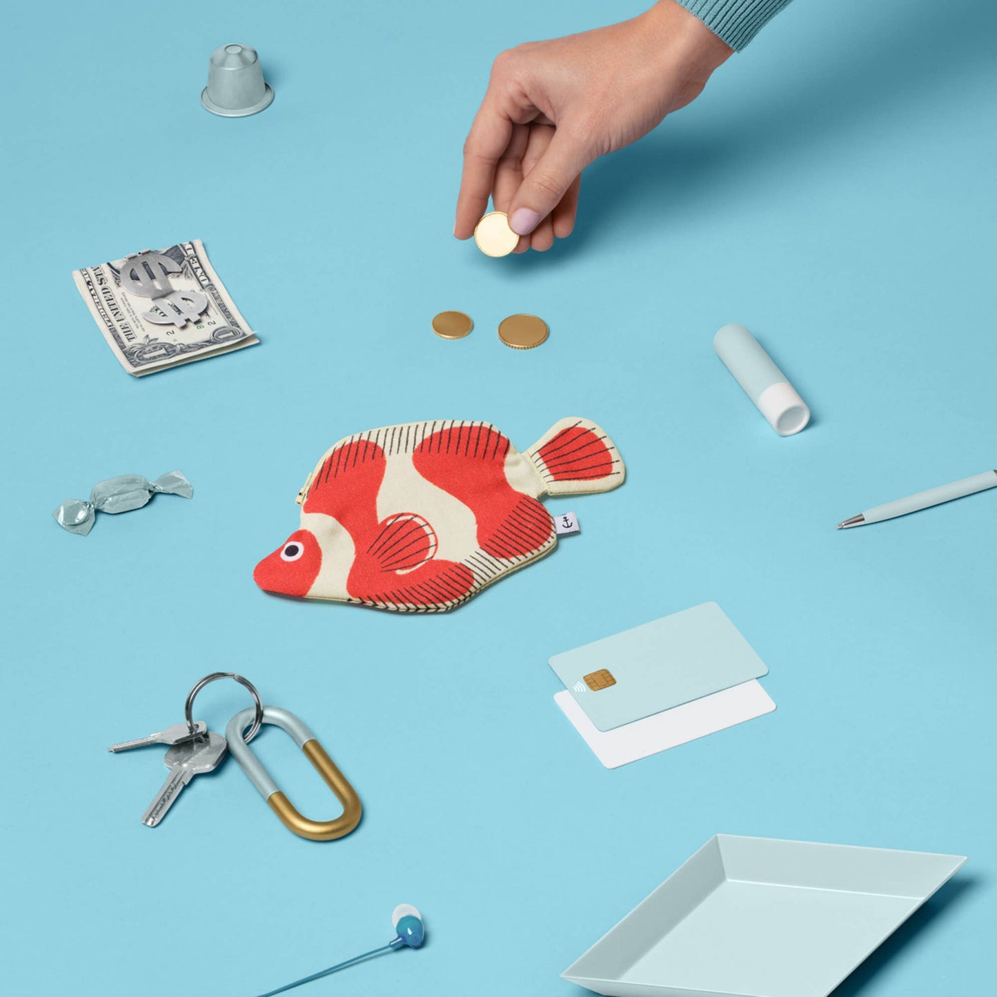 Red and white clownfish-shaped pouch on a blue background with coins and keys.
