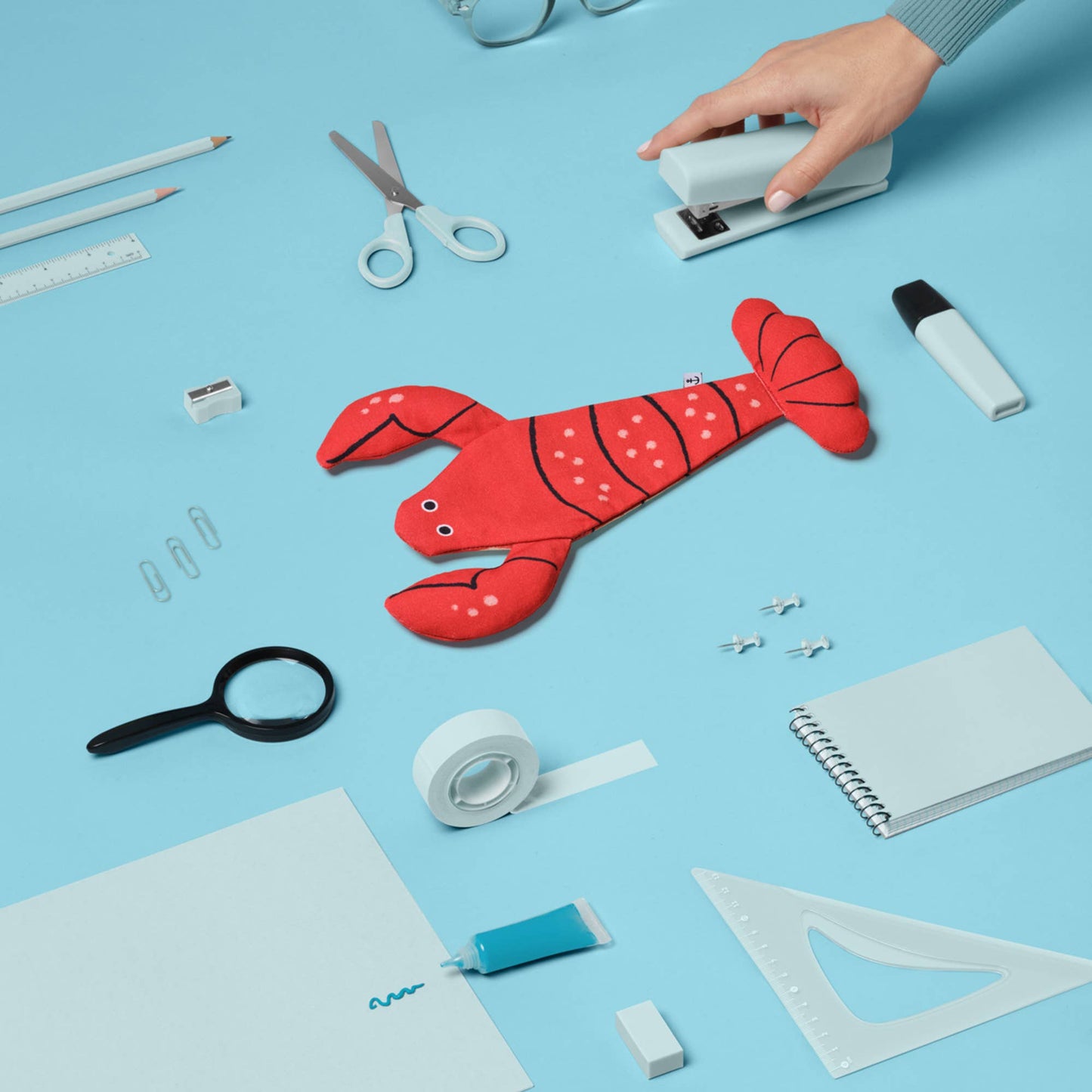 Red lobster-shaped pouch on a blue background with stationery items.