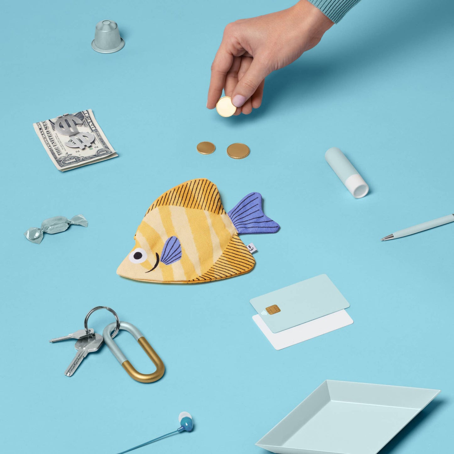 Fish-shaped pouch with various small items on a blue background