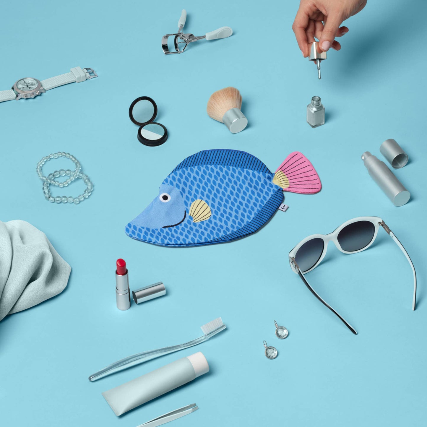 Collection of small items including a fish-shaped pouch, sunglasses, and lip products on a blue background