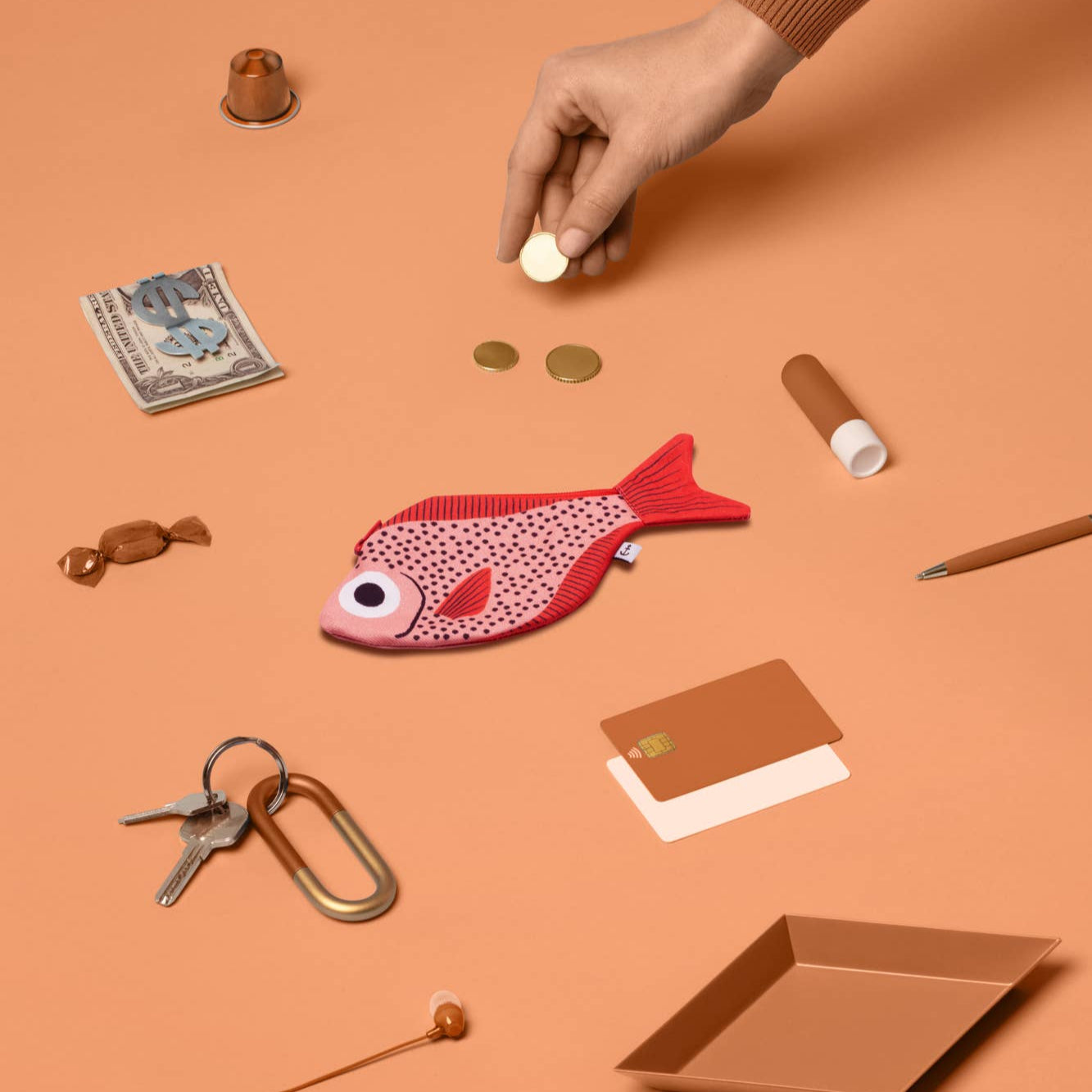 Pink fish-shaped pouch with coins on an orange surface