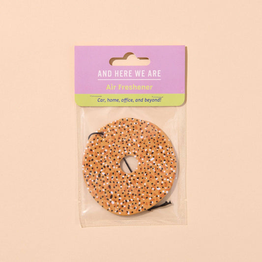 Everything bagel air freshener in clear packaging with purple label on beige background