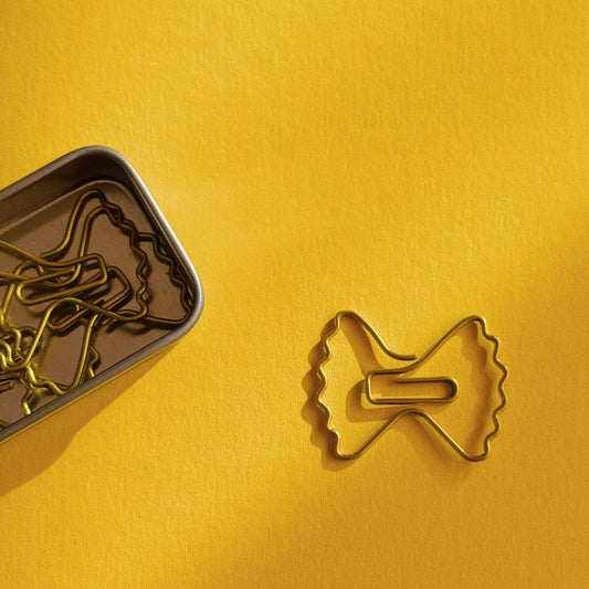 Paper clips shaped like farfalle pasta in a small tin can for storage