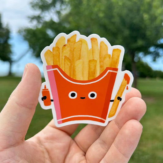 Sticker of a cute cartoon-style French fry container held in a hand with a natural background.