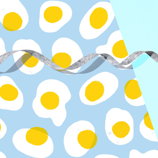 sheet of gift wrap with a sky blue background and fried eggs all over