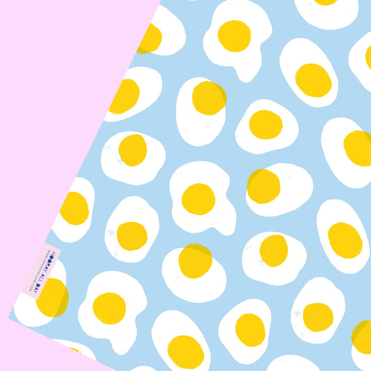 sheet of gift wrap with a sky blue background and fried eggs all over