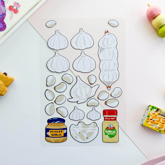 Set of garlic-themed stickers with clear backing on a white surface with small items around.