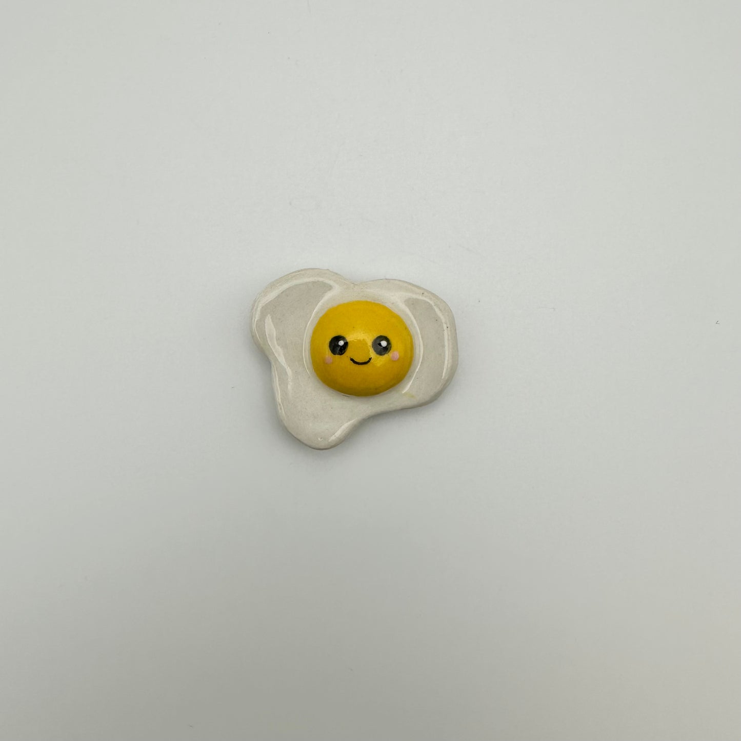 small ceramic fried egg magnet with a smiley face painted on