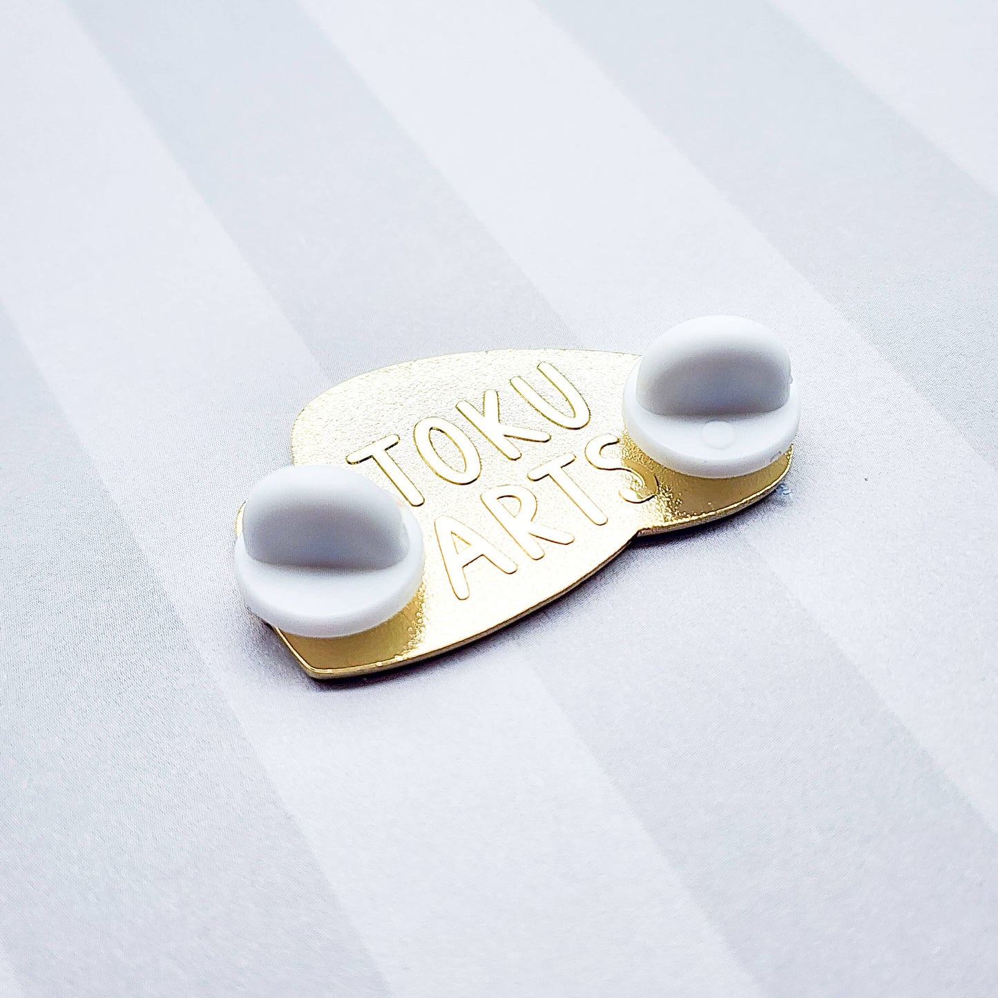 Back of the caviar enamel pin, showcasing the brand name and two white, rubber backings on it