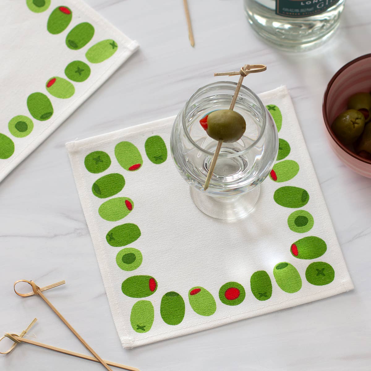 Cloth cocktail napkin with olive design on a white surface with a martini with an olive