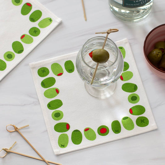 Cloth cocktail napkin with olive design on a white surface with a martini with an olive