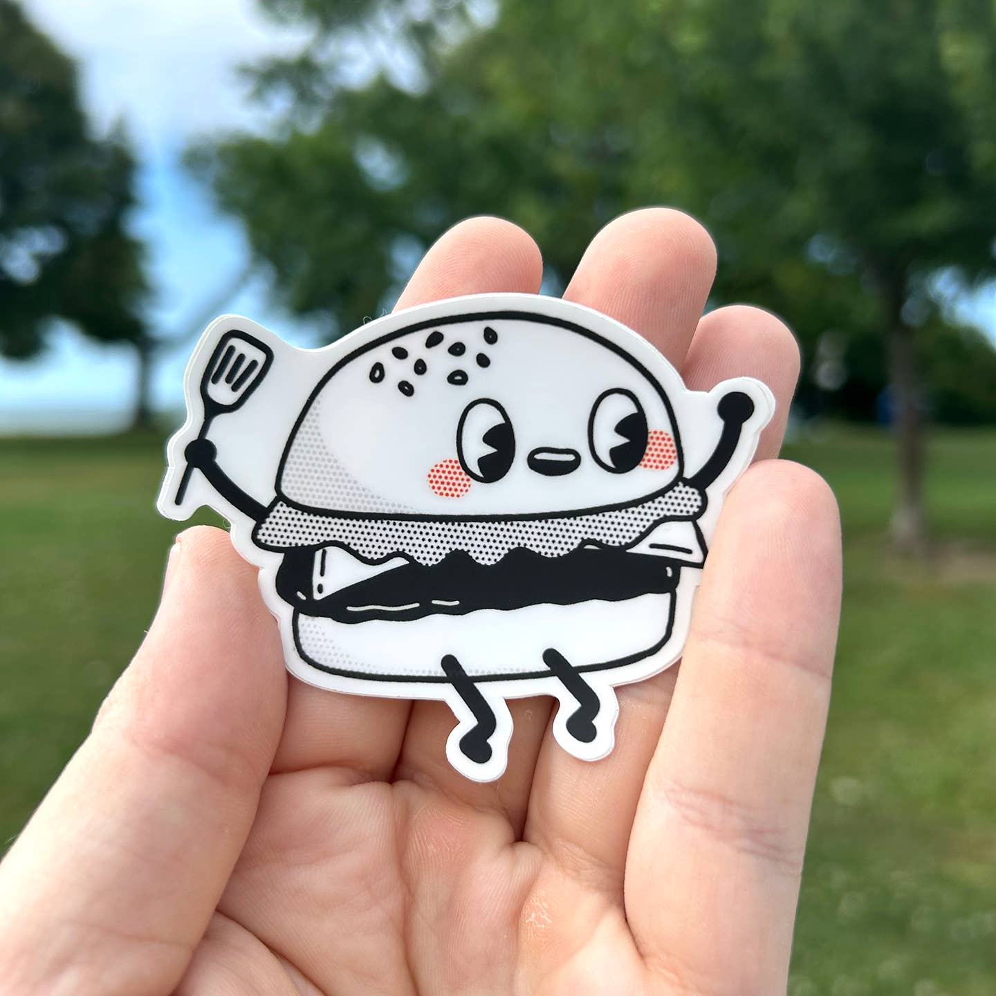 Cartoon hamburger sticker held in a hand with a blurred green outdoor background