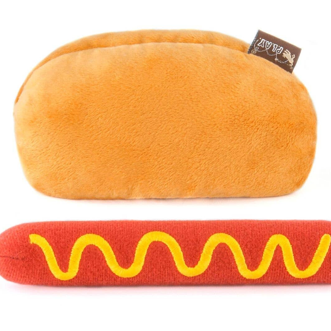 Plush hot dog toy with bun and red sausage with yellow mustard on a white background