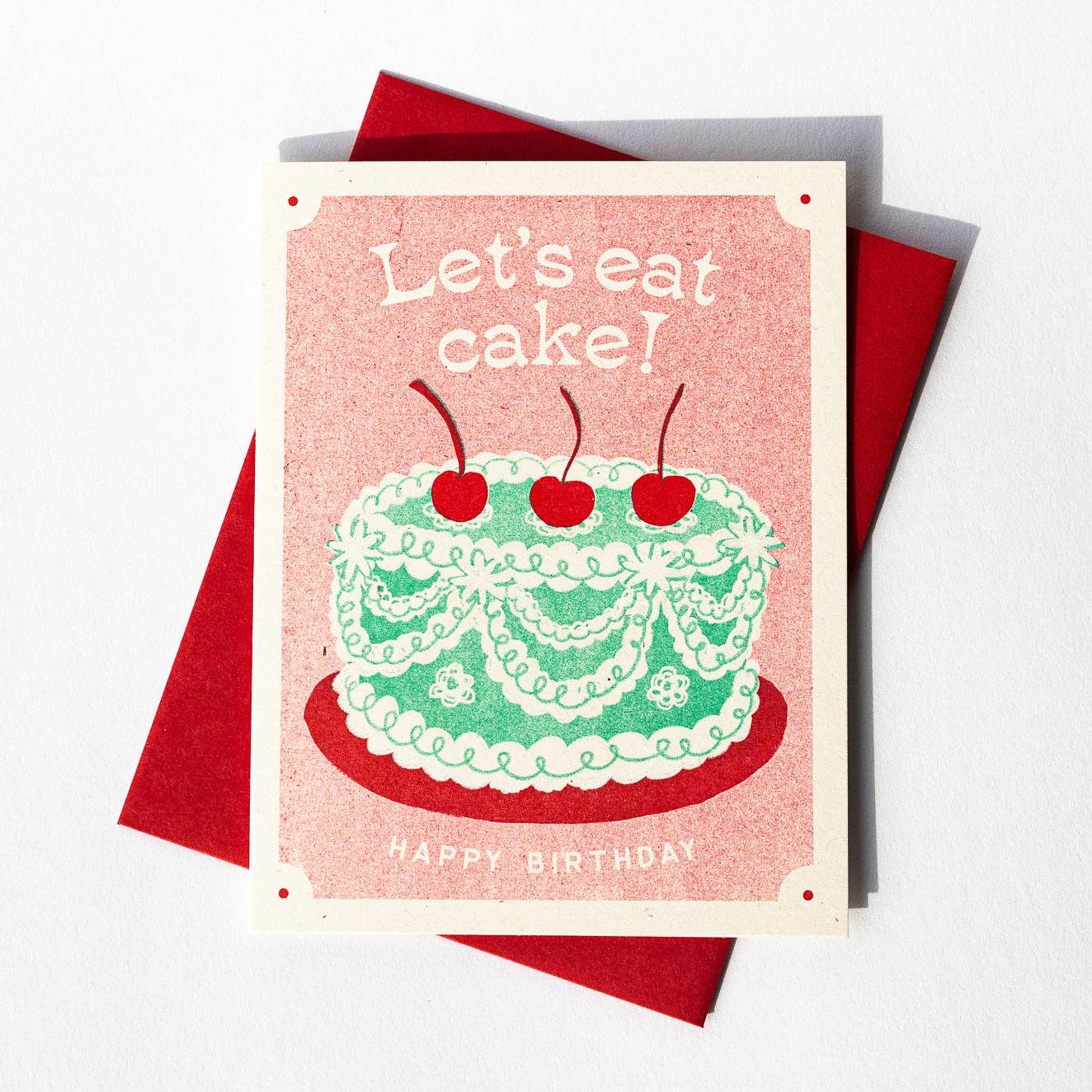 Birthday card with green frilly cake, decorated with ribboned icing and three red cherries on the top. Text reads "Let's eat cake! Happy birthday"