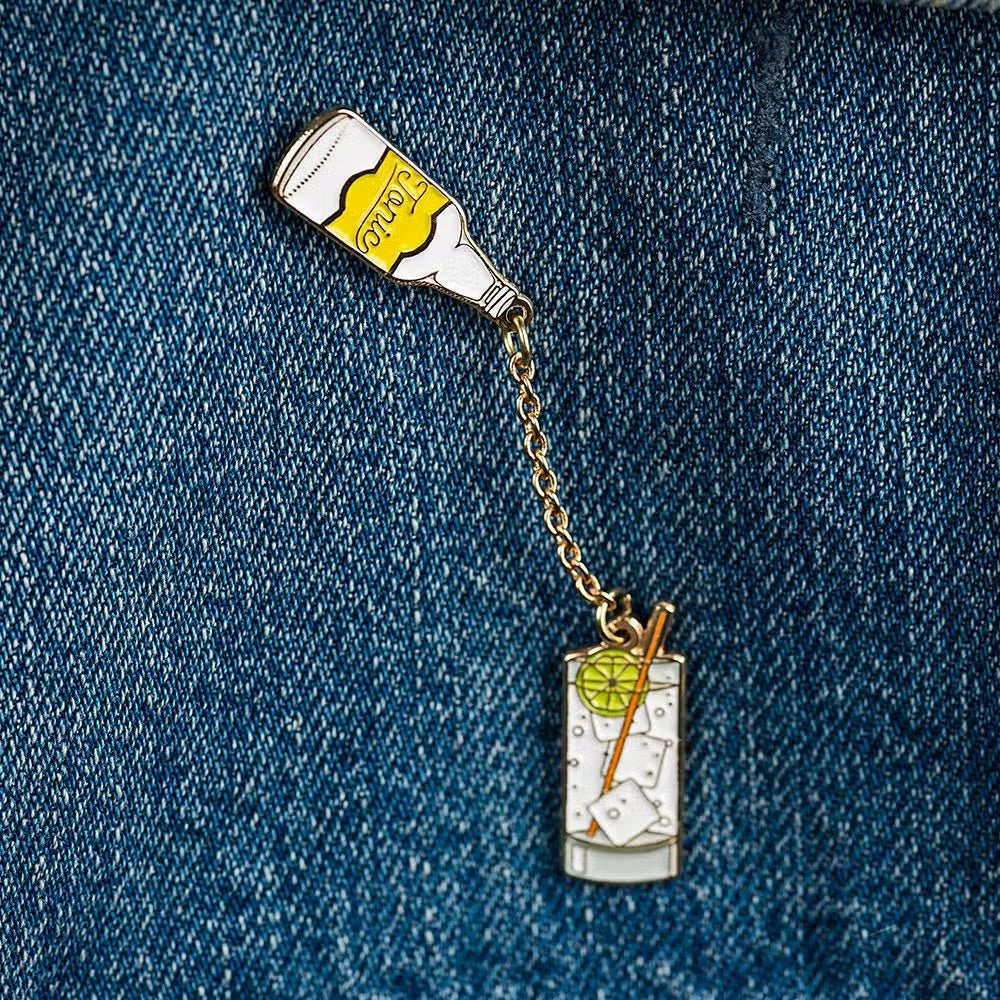 gin and tonic enamel pin -- tonic bottle is connected to glass filled with ice, gin & tonic, lime and a straw and is placed above the glass to look like it's pouring into the glass