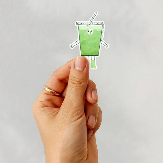 Hand holding a iced matcha cup with a straw and smiley face on a light gray background