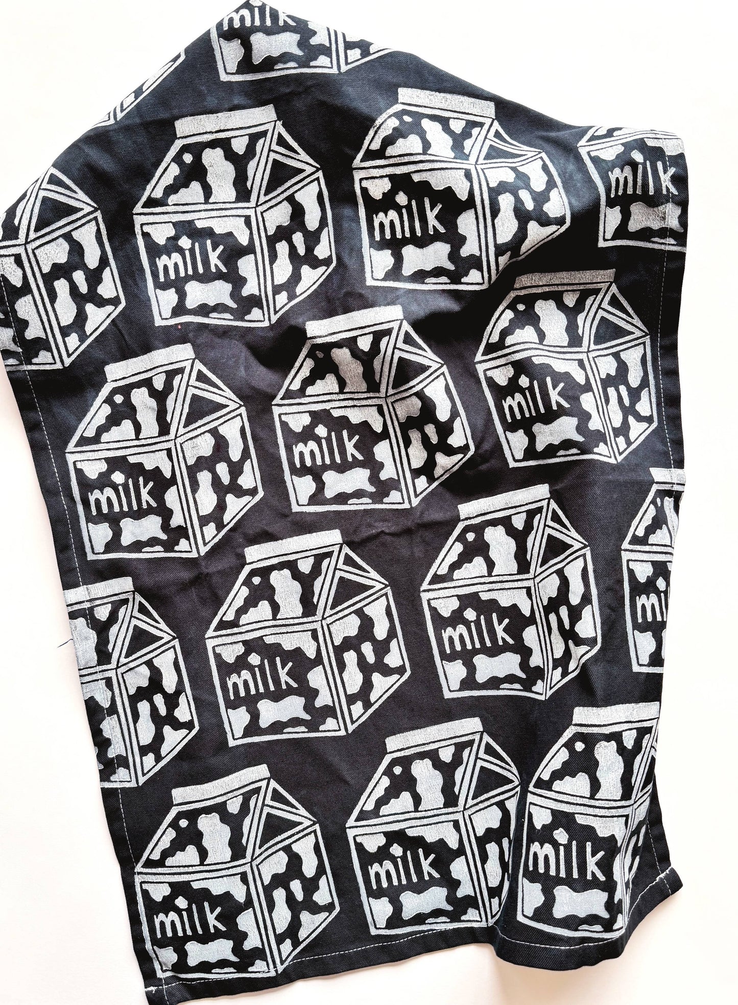black tea towel with a repeated pattern of cow print milk cartons