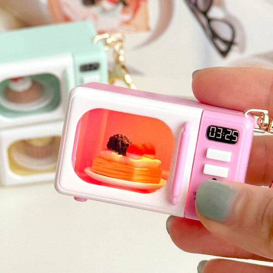 Small pink mini microwave keychain with digital clock and a cake display held by a hand.