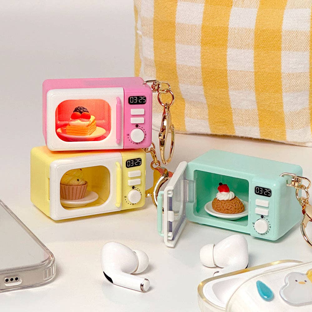 Three colorful microwave-shaped keychains on a white surface with a yellow and white striped towel in the background.