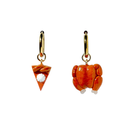 Two mismatched earrings, one pumpkin pie charm and one turkey charm, with gold hoops on a white background