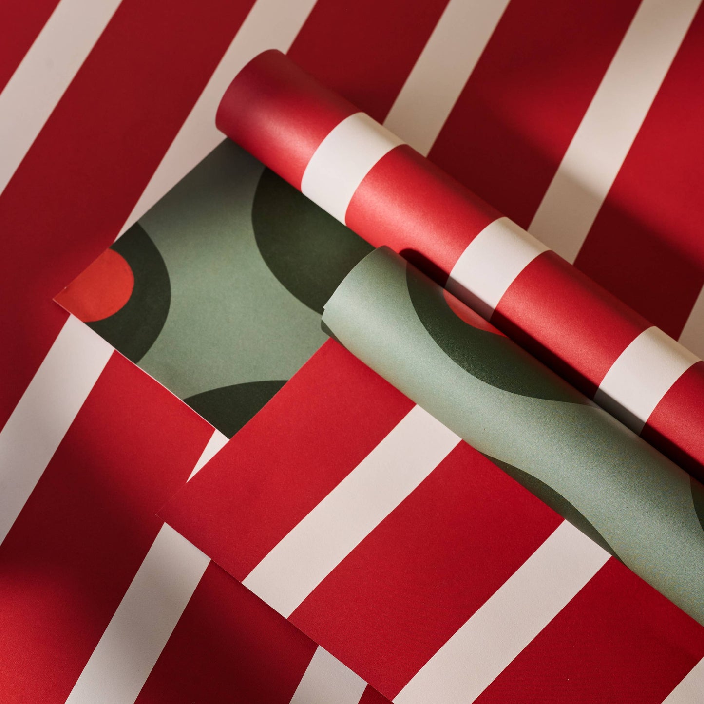 Two rolls of wrapping paper -- one red and white stripes and the other green olives on a red background with white stripes.