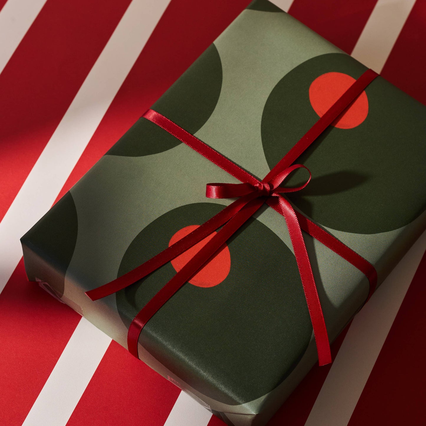 Green gift box with a stuffed green olive pattern and a red ribbon on a red and white striped background