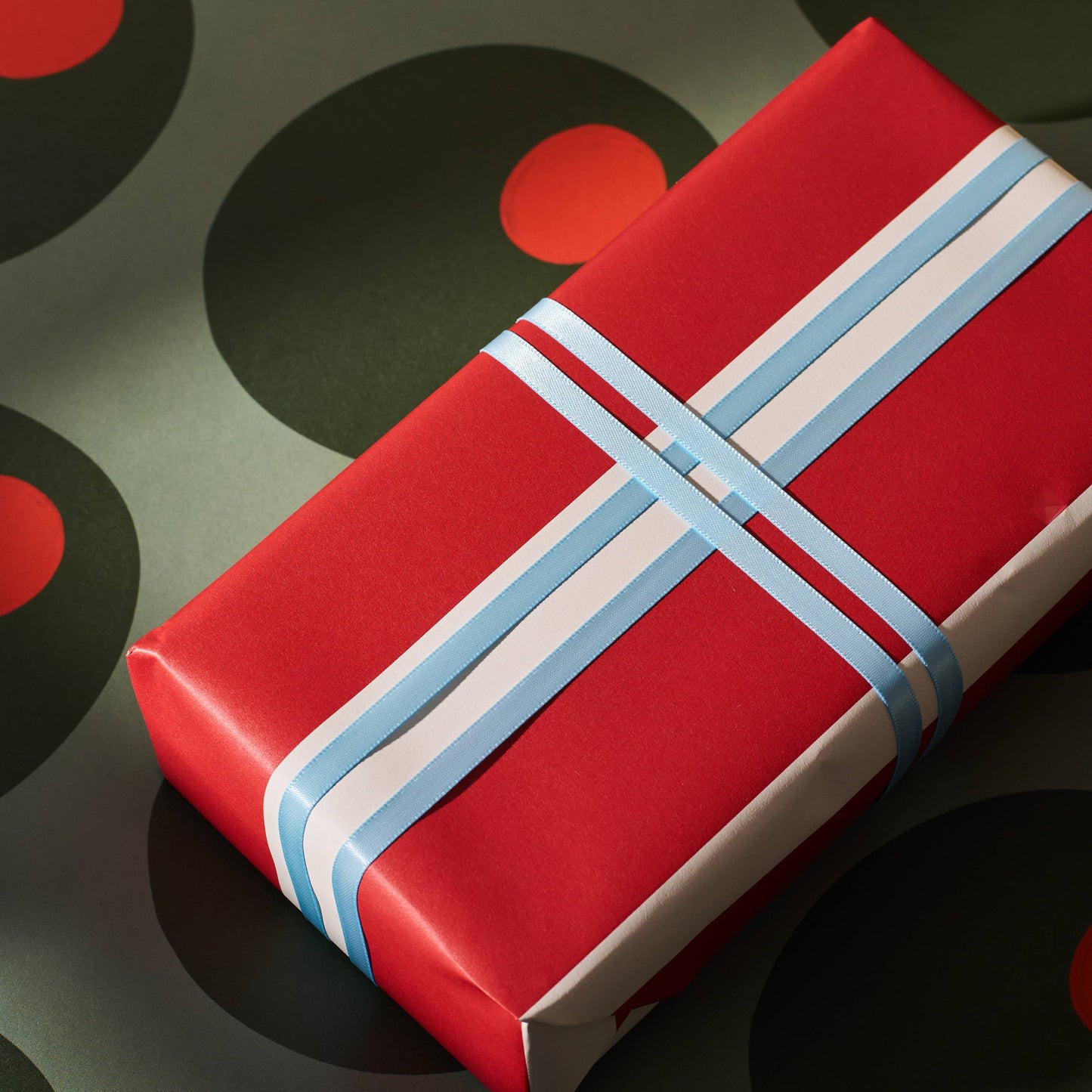 Red gift box with blue ribbon on ann olive patterned background