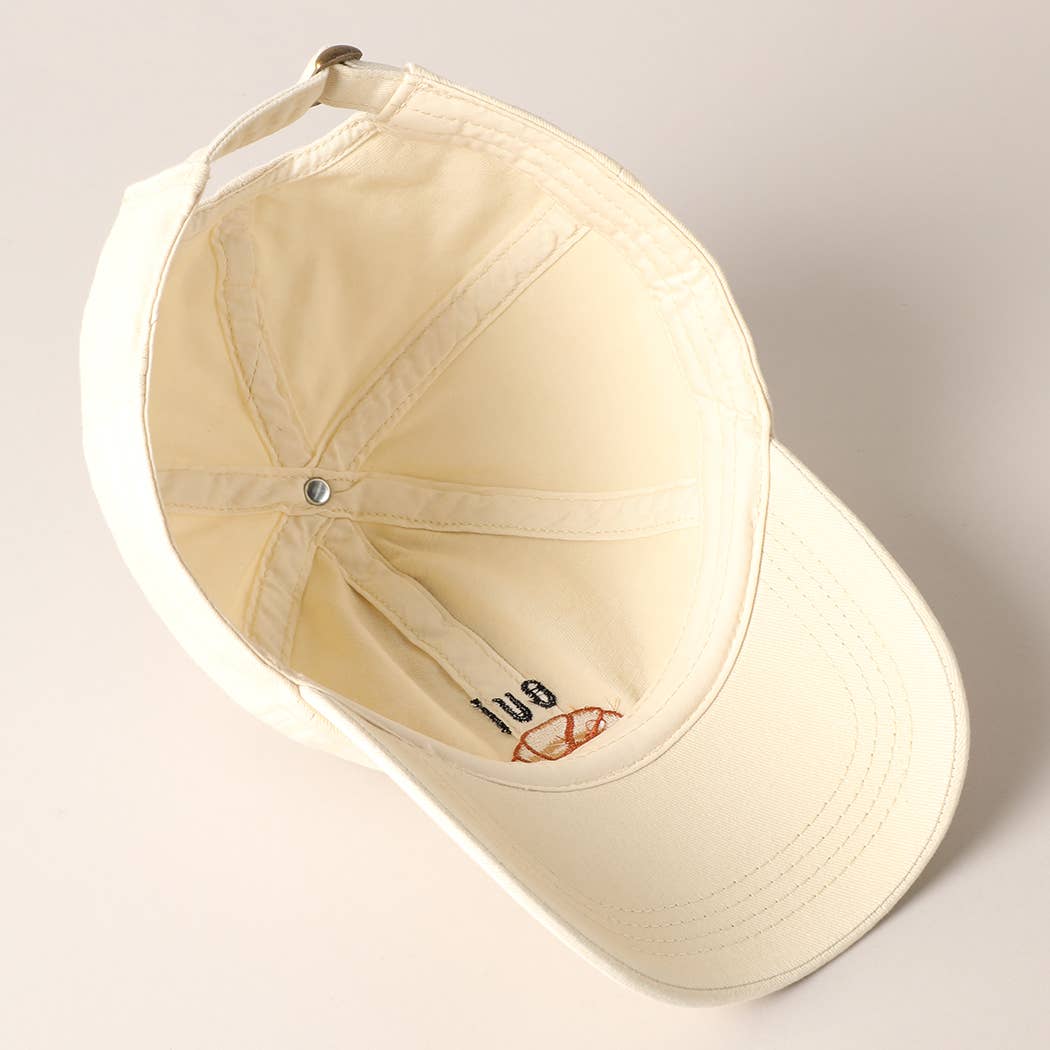 A cream baseball cap with 'oui' written on it and an embroidered croissant below the text.