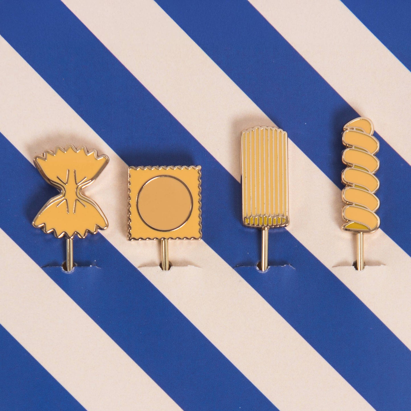 Four gold-colored pasta themed cocktail picks on a blue and white striped background