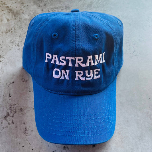blue baseball cap with white embroidered text that reads "pastrami on rye"