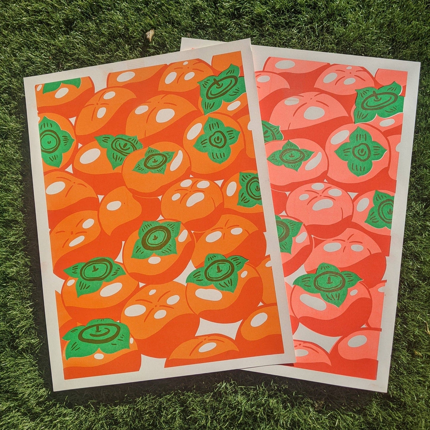 Two art prints with a pattern of orange persimmons5 and green leaves on a grass background