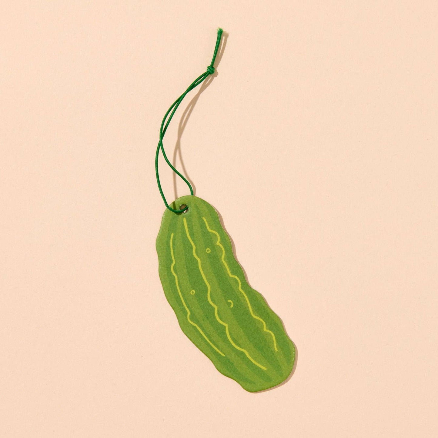 Green pickle-shaped air freshener on a beige background