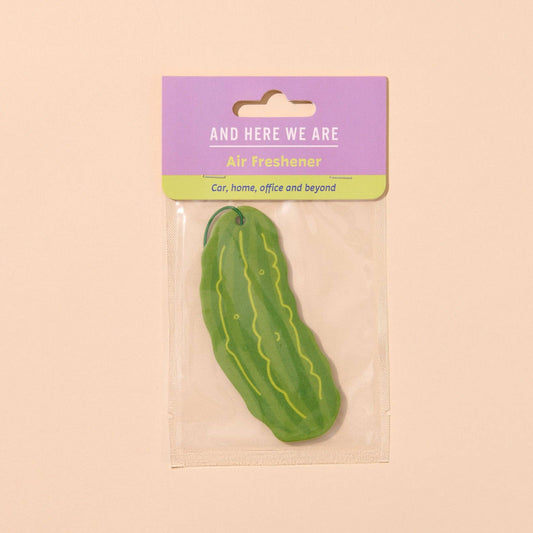 Green pickle-shaped air freshener with a purple label on a beige background