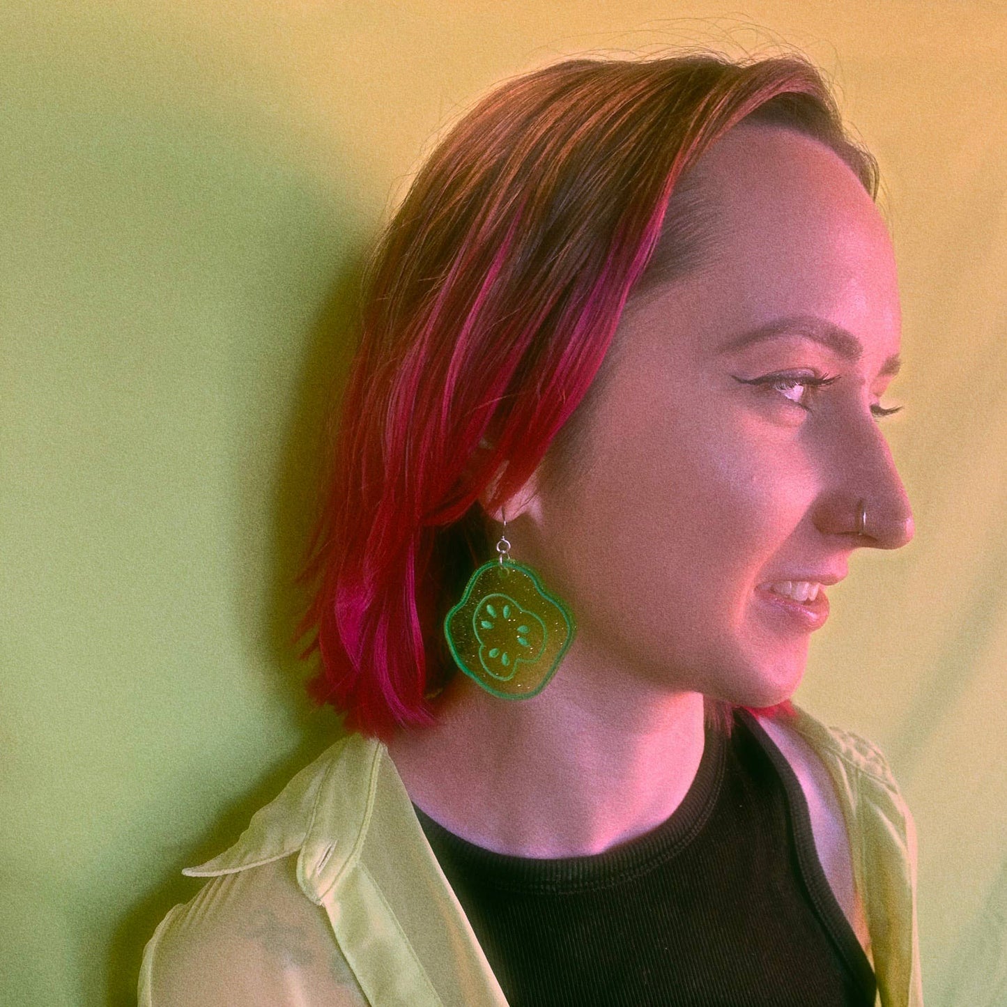 Glittery, green, acrylic, sliced pickle earrings on fish hook backings. Seen here being worn on a person