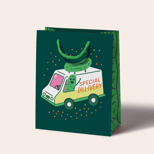 Green gift bag with a pickle-themed delivery truck illustration on a beige background