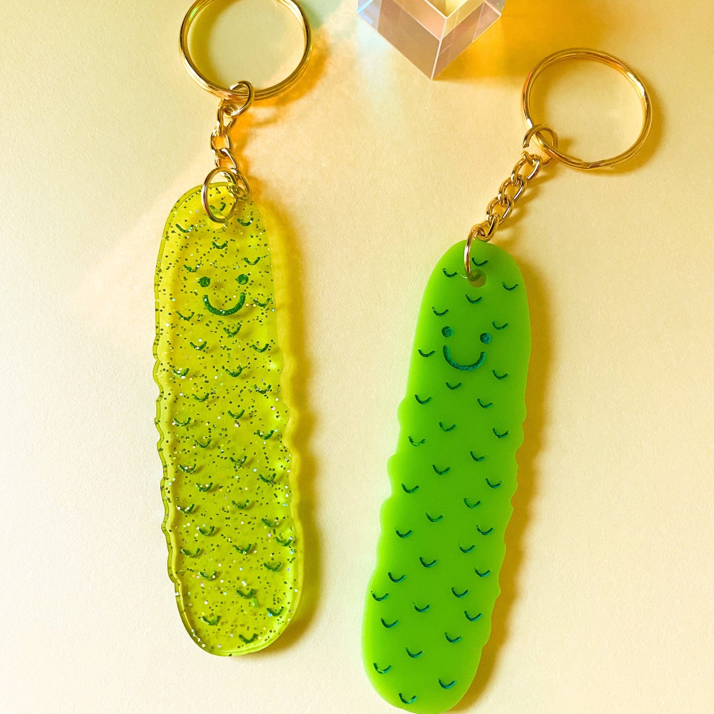Two pickle-shaped acrylic keychains on a light yellow background
