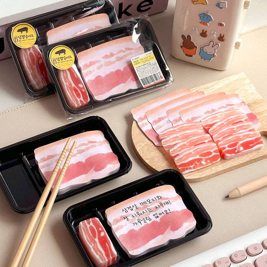 Eraser and memo notes that look like sliced pork belly on a table with chopsticks and a cutting board.