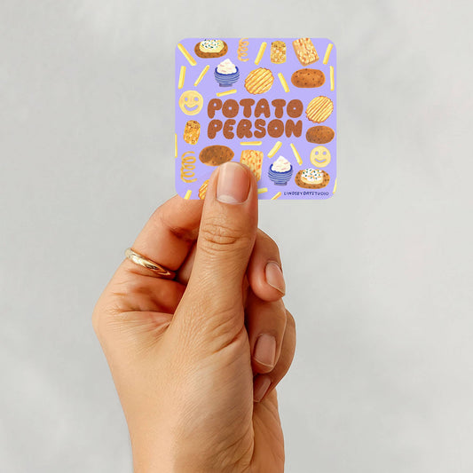 Hand holding a sticker with 'Potato Person' text against a light gray background
