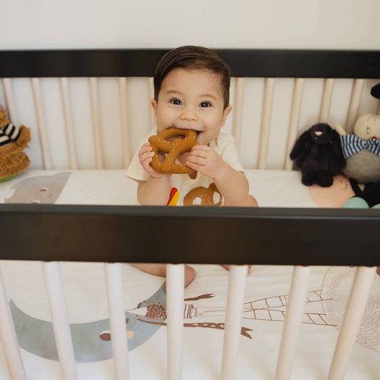 Baby in a crib with the pretzel teether in his mouth