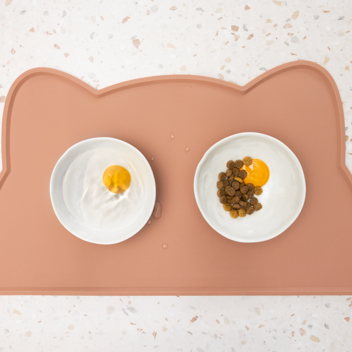 Cat-shaped mat with two egg bowls filled with food and water on a light background