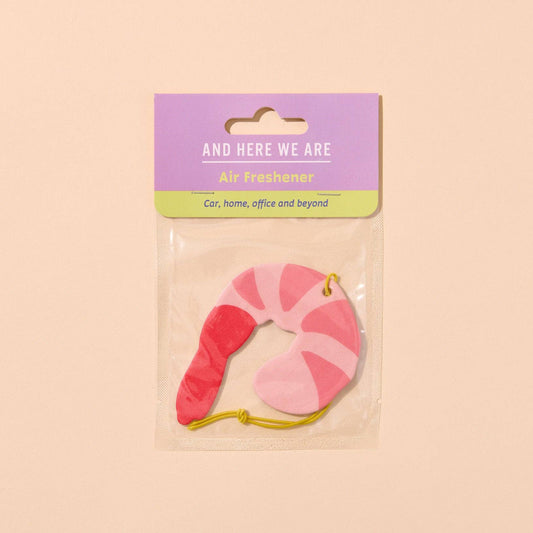 Shrimp shaped air freshener on a beige background with 'And Here We Are' branding.