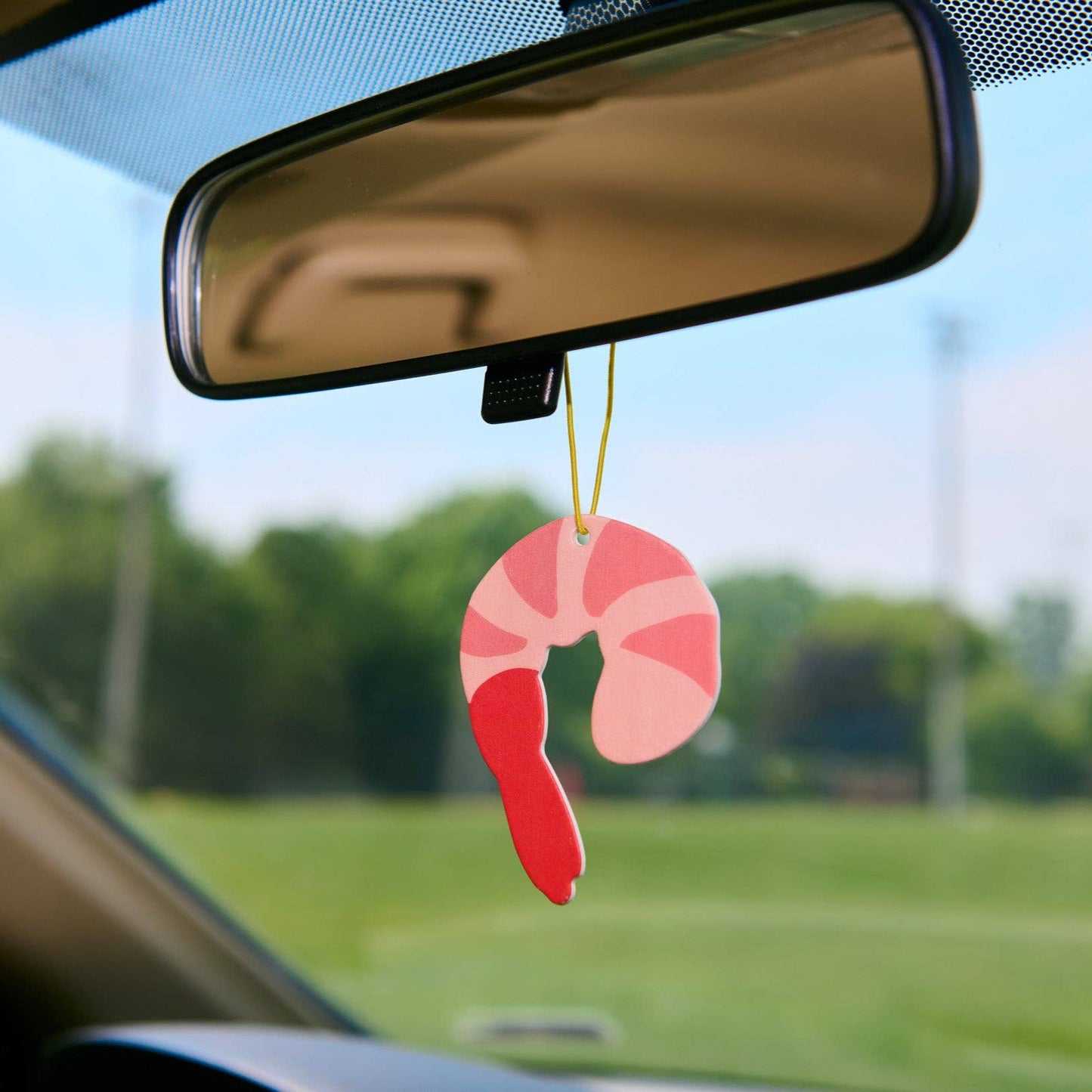 Car air freshener shaped like a shrimp hanging from a car's rearview mirror.