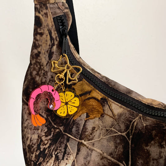 Camouflage sling bag with colorful keychain/charms on a neutral background