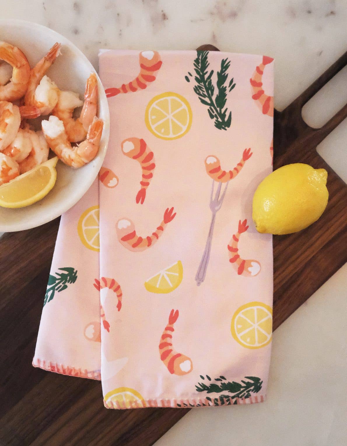Kitchen tea towel, light pink/salmon in color with a design of illustrated lemon halves and wedges, shrimp, cocktail fork and herbs